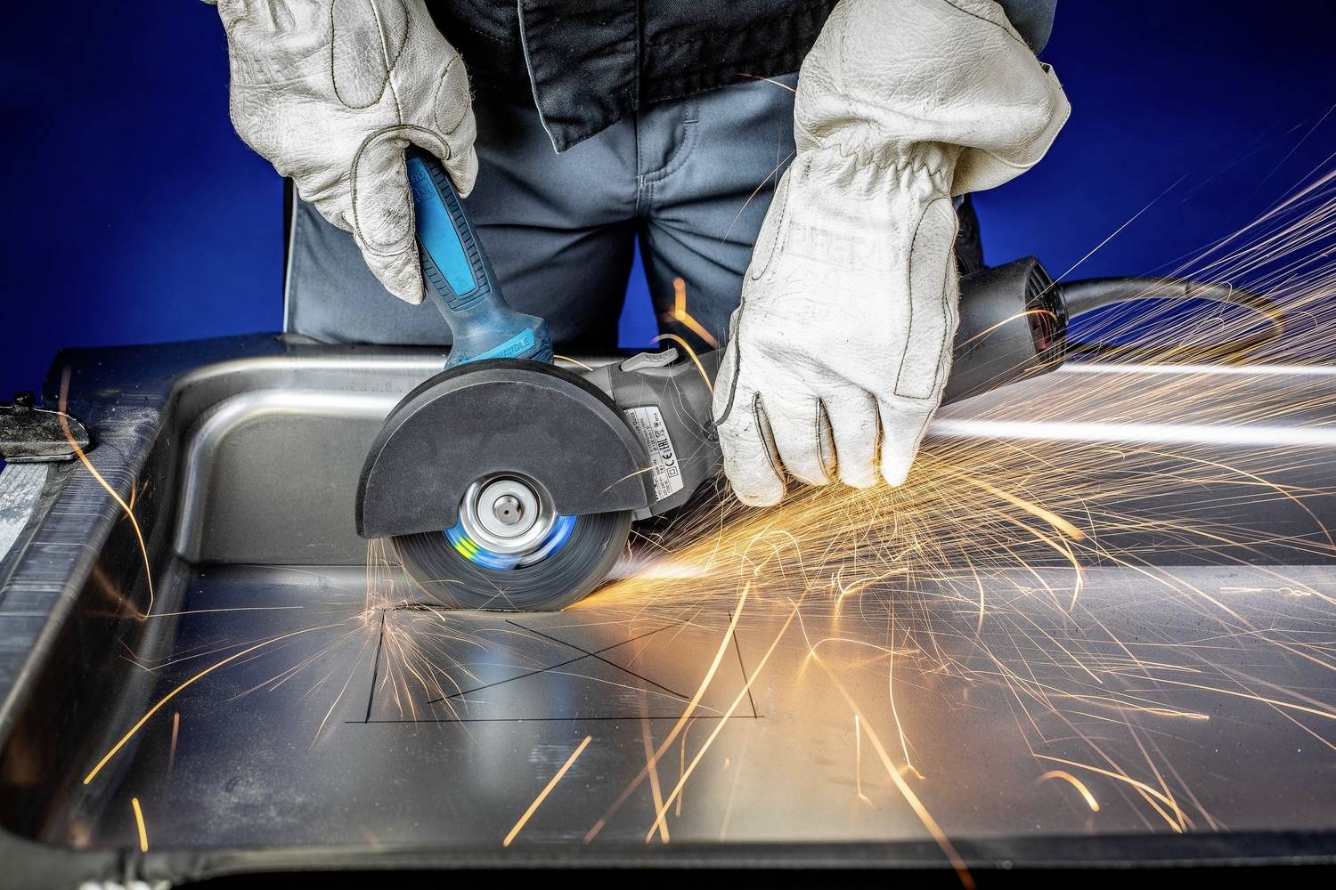 Osoba v ochranných rukavicích řeže kov úhlovou bruskou, přičemž na stranu odlétávají jiskry.