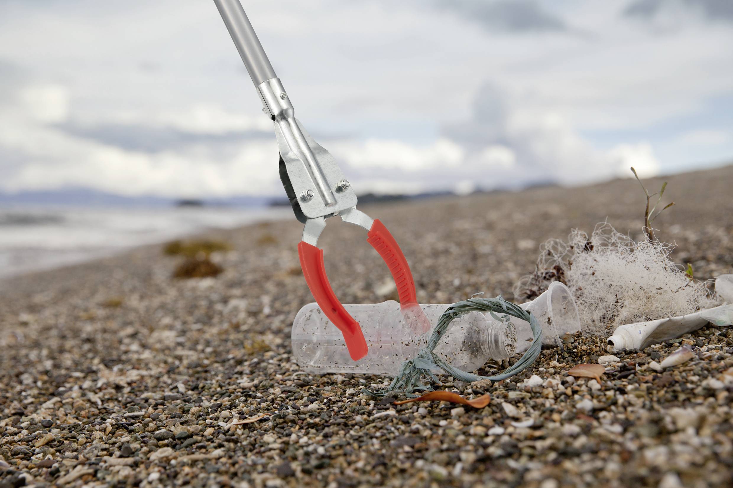 Úklidový stroj zvedá plastové láhve a odpadky na pláži. Moře a obloha v pozadí. Environmentální uvědomění a úklid pobřeží.