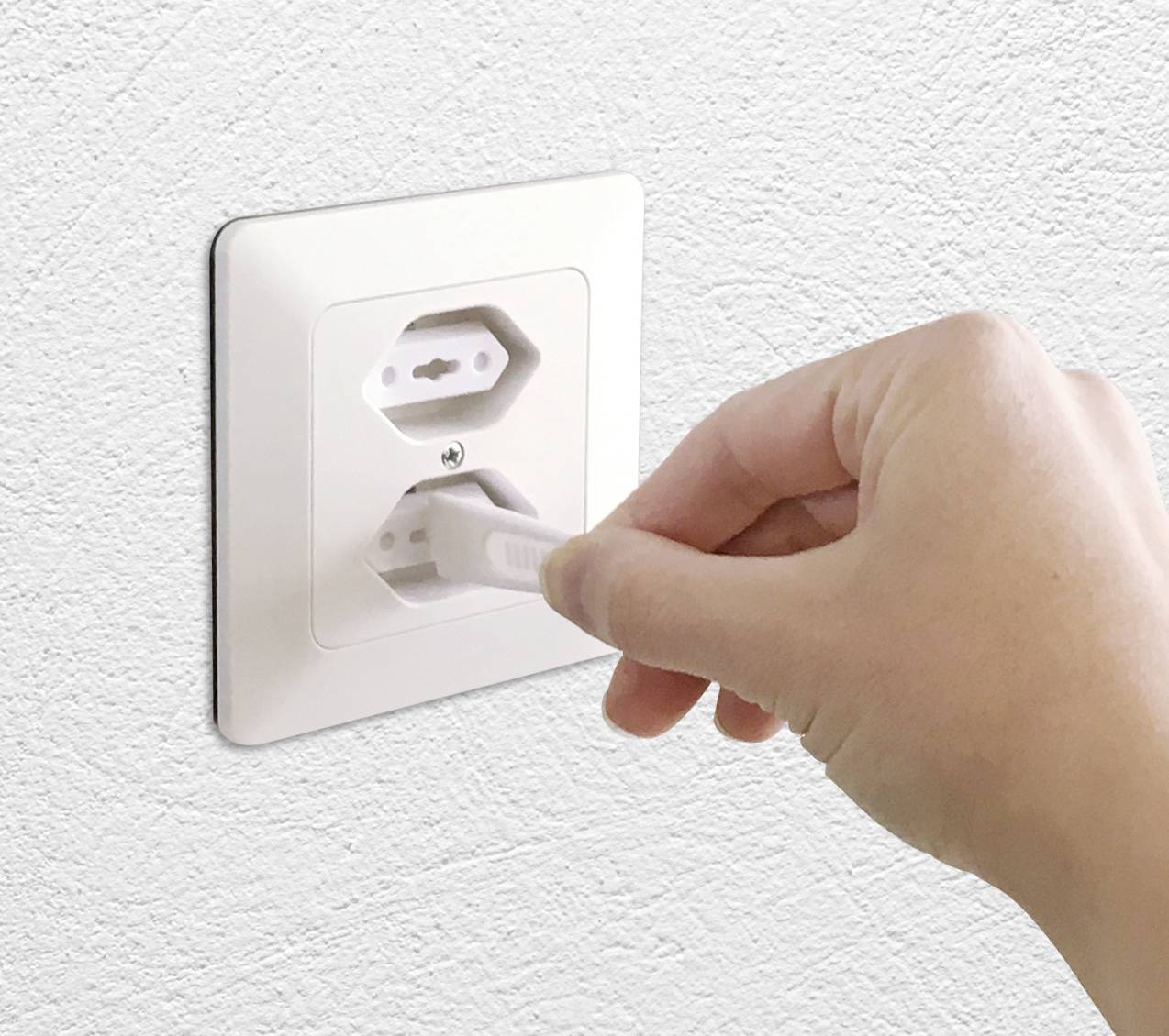 Ruka zasunuje bílou zástrčku do bílé elektrické zásuvky na bílé stěně.