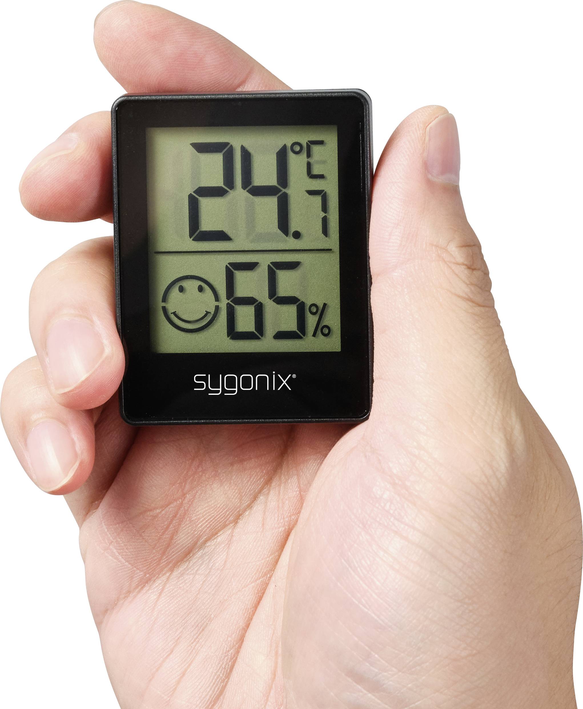 Ruka drží digitální teploměr s vlhkoměrem. Ukazuje teplotu '24,7°C' a vlhkost vzduchu '65%' s úsměváckou ikonou.