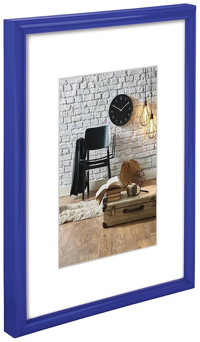 Zarámovaný obraz ukazuje černé hodiny na bílé cihlové zdi, vedle nichž stojí židle a kufr na dřevěné podlaze.