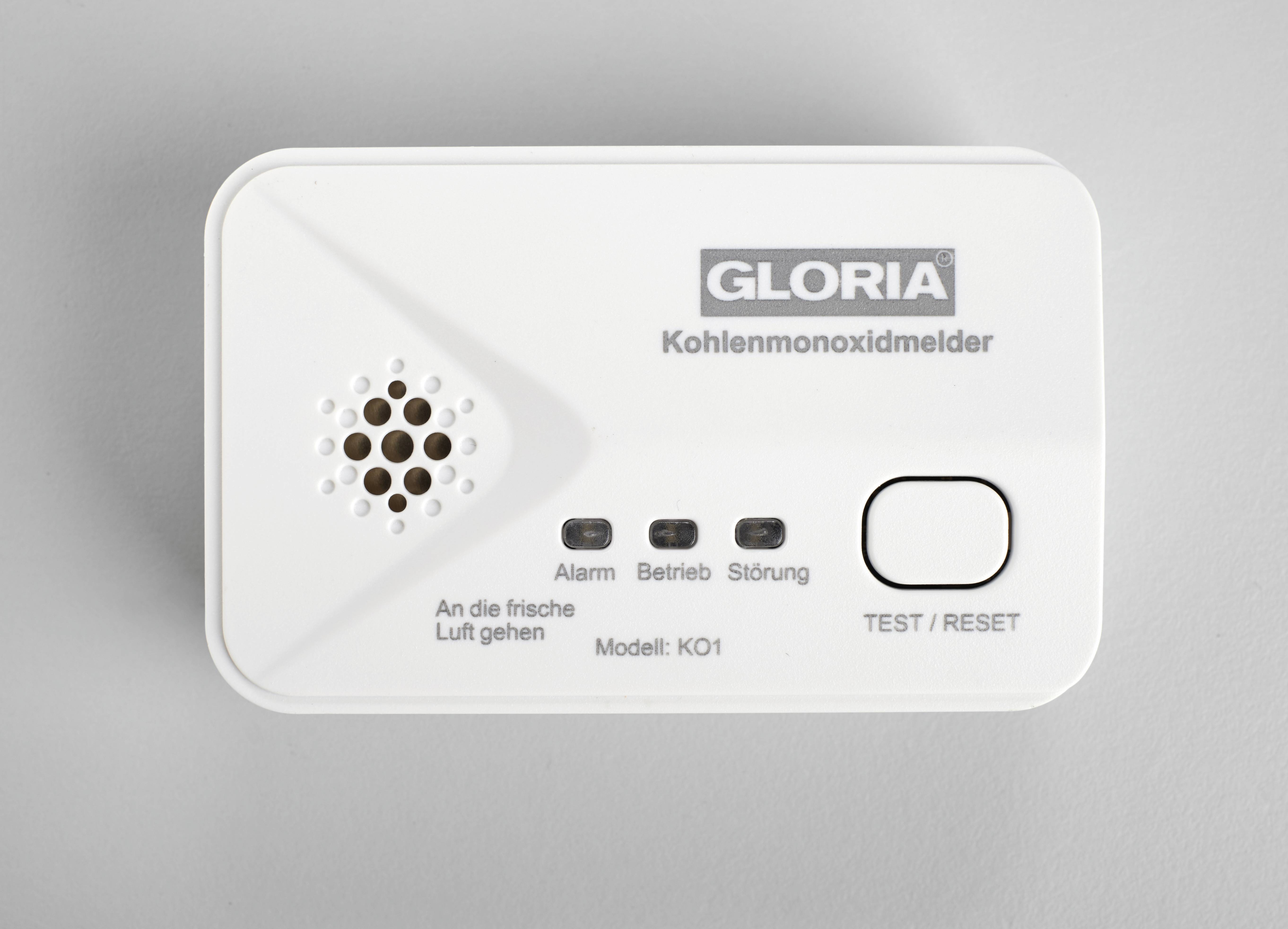 Bílý detektor oxidu uhelnatého s nápisem 'GLORIA Detektor oxidu uhelnatého'. Tlačítka pro alarm, provoz, poruchu a test/reset.