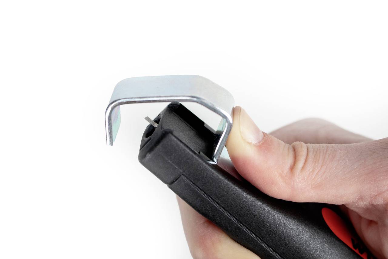 Ruka drží odstraňovač svorek. Kovové čelisti jsou ohnuty přes špičku, aby odstranily sponku.