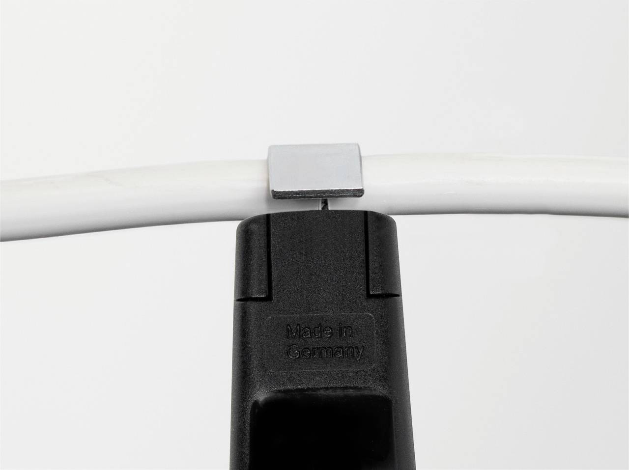 Černý stojan drží bílý kabel. Na stojanu je nápis „Made in Germany". V pozadí je neutrální, světlý podklad.