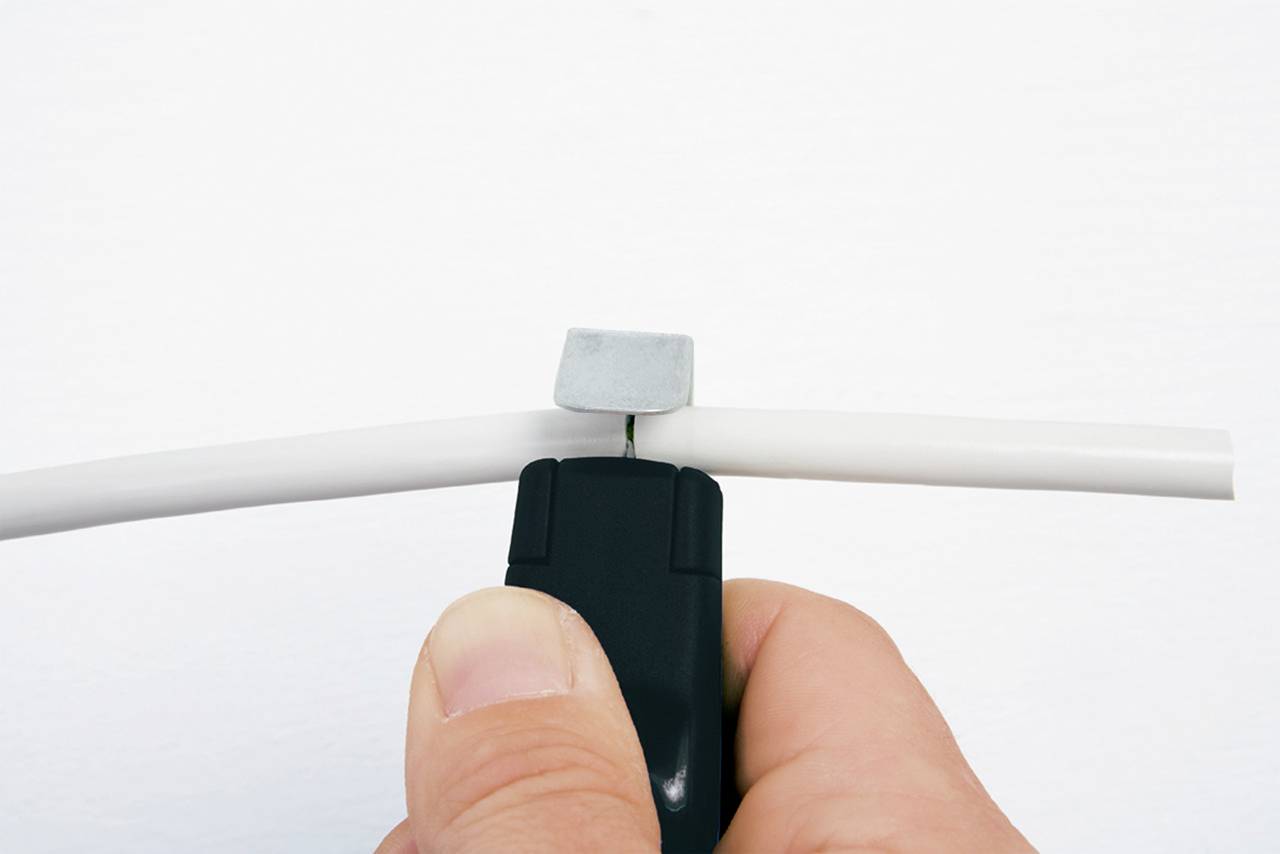 Detailní záběr ruky, která používá nástroj ke stříhání kabelu. Nástroj je černý a kabel je bílý.