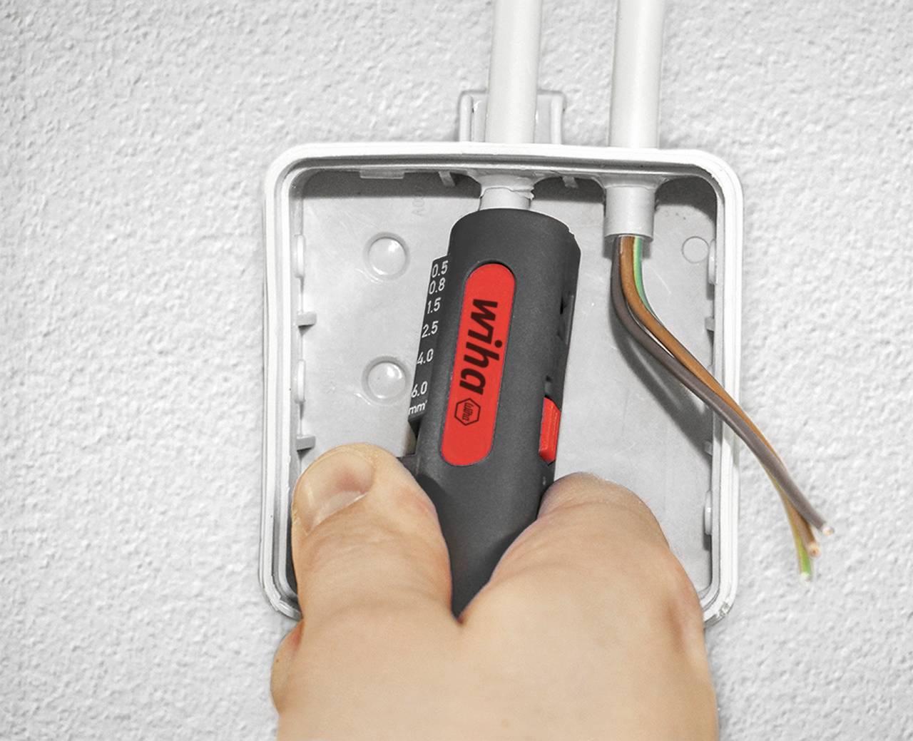 Jedna ruka drží zkoušečku napětí u otevřené elektrické rozvodné skříně s viditelnými kabely.
