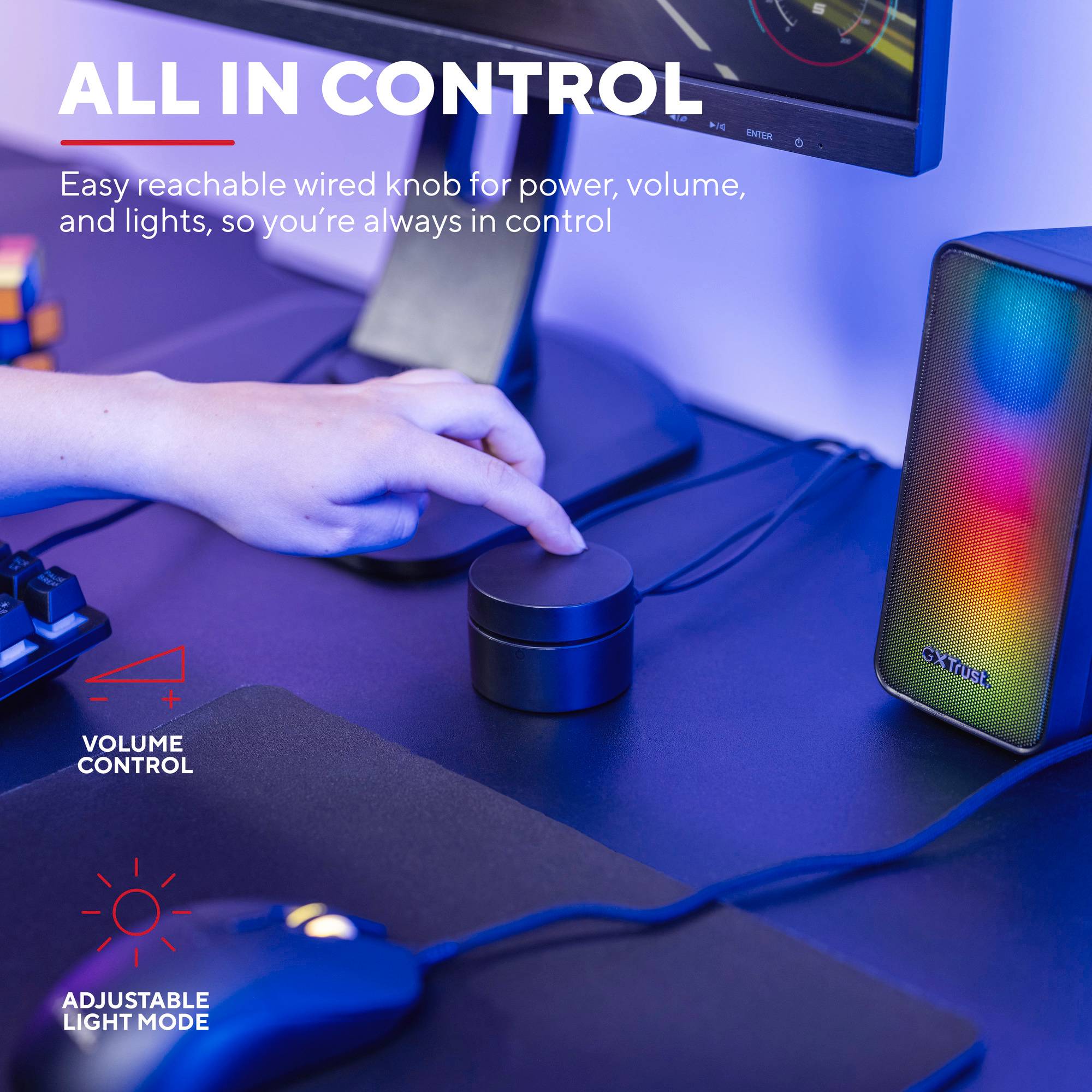 'Všechno pod kontrolou': Ruka otáčí regulátorem hlasitosti na stole s RGB reproduktory a monitorem v pozadí.
