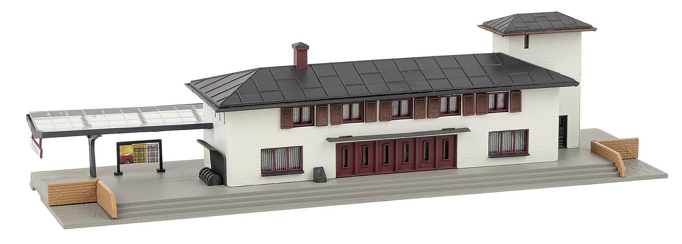 Miniaturní model moderního dvoupatrového nádraží s krytým nástupištěm a červenými okny.