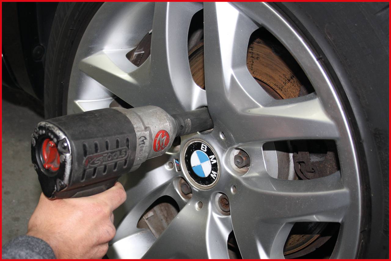 Ruka používá rázový utahovák k povolení nebo utažení matice kola automobilu s logem BMW.