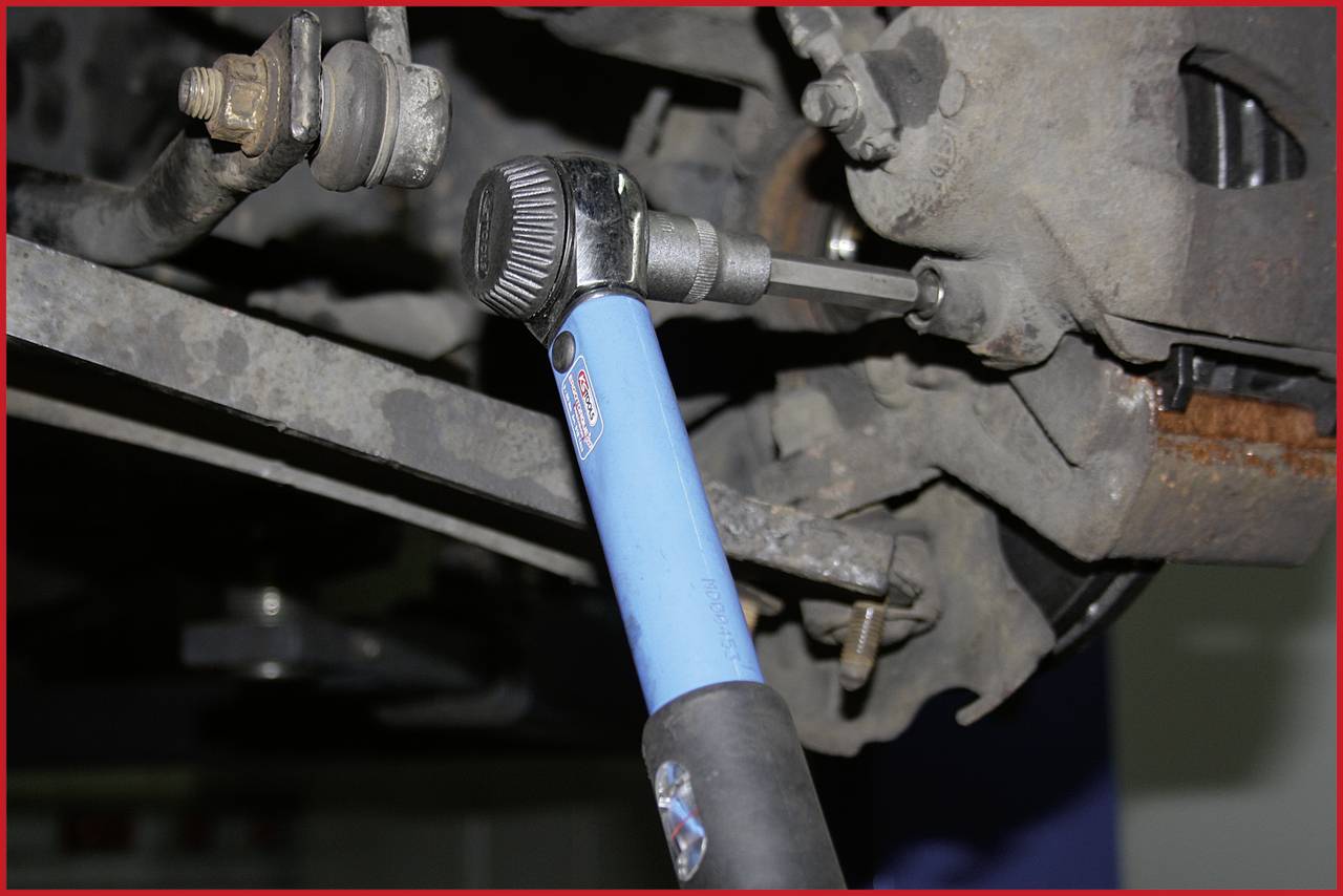 Detailní záběr momentového klíče pracujícího na součásti automobilu pod vozidlem, pravděpodobně v rámci údržby nebo opravy.