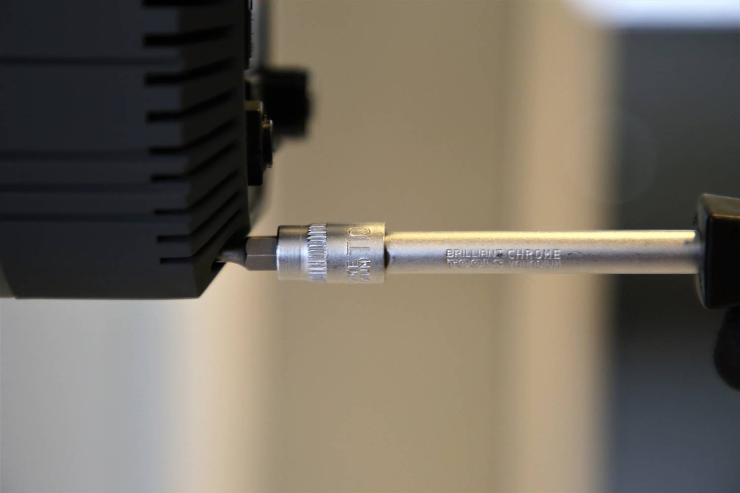 Šroubovák utahuje šroub do černého zařízení. Zaměření je na nástroji a šroubu.