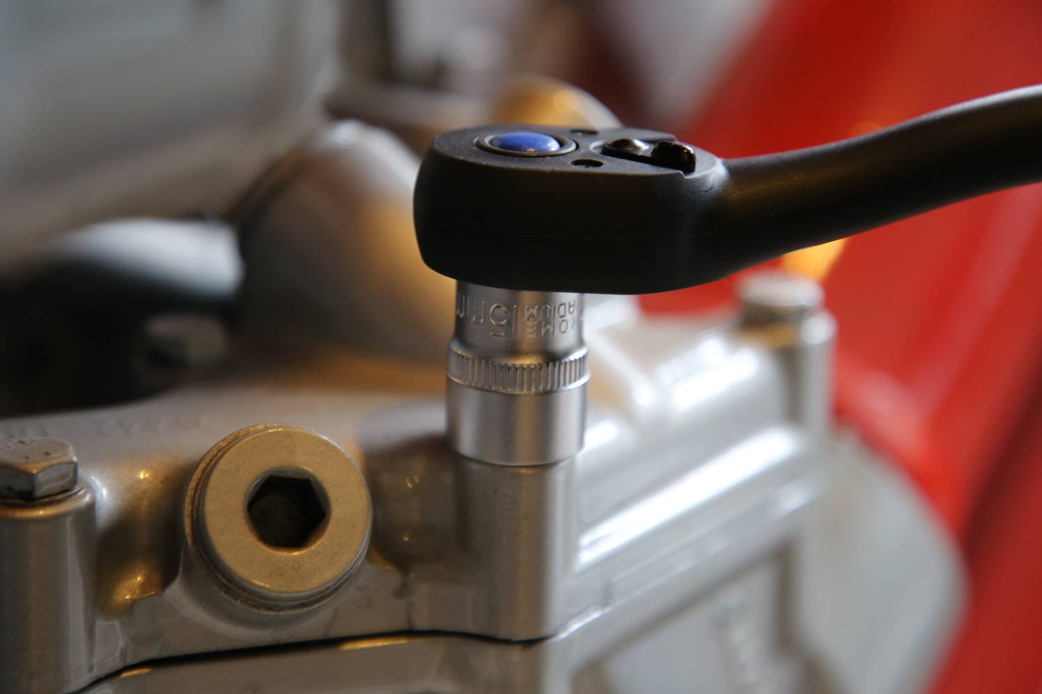 Detailní záběr francouzského klíče, který pracuje na šroubu motoru nebo strojní součásti. Důraz je kladen na přesnost.