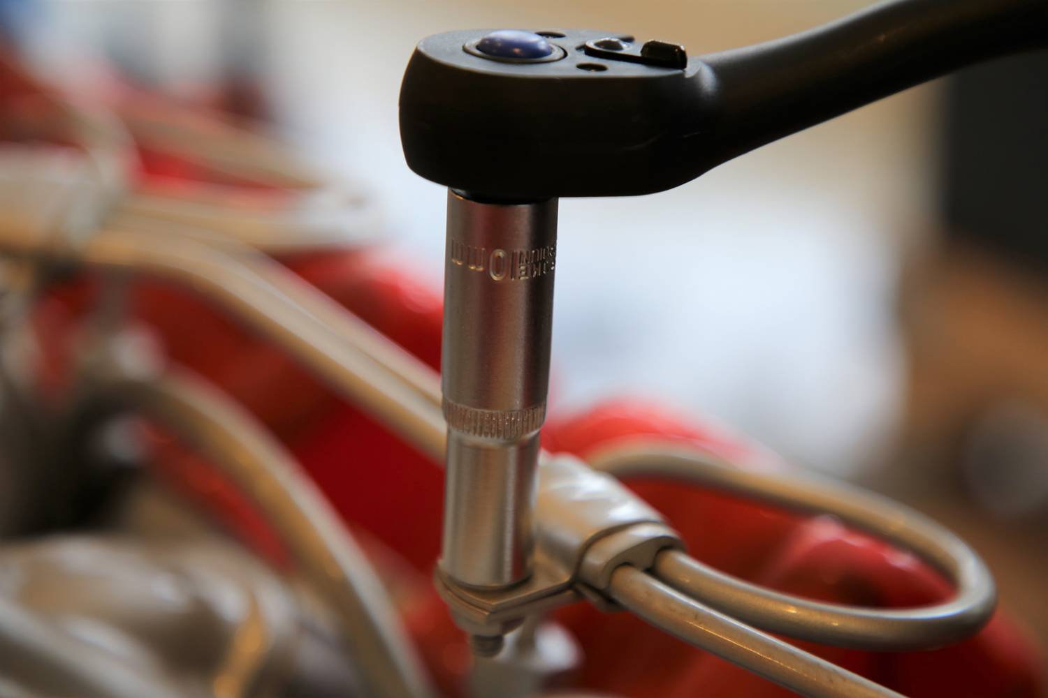 Detailní záběr momentového klíče, který je nasazen na šroub mechanického zařízení. Měkké detaily v pozadí.