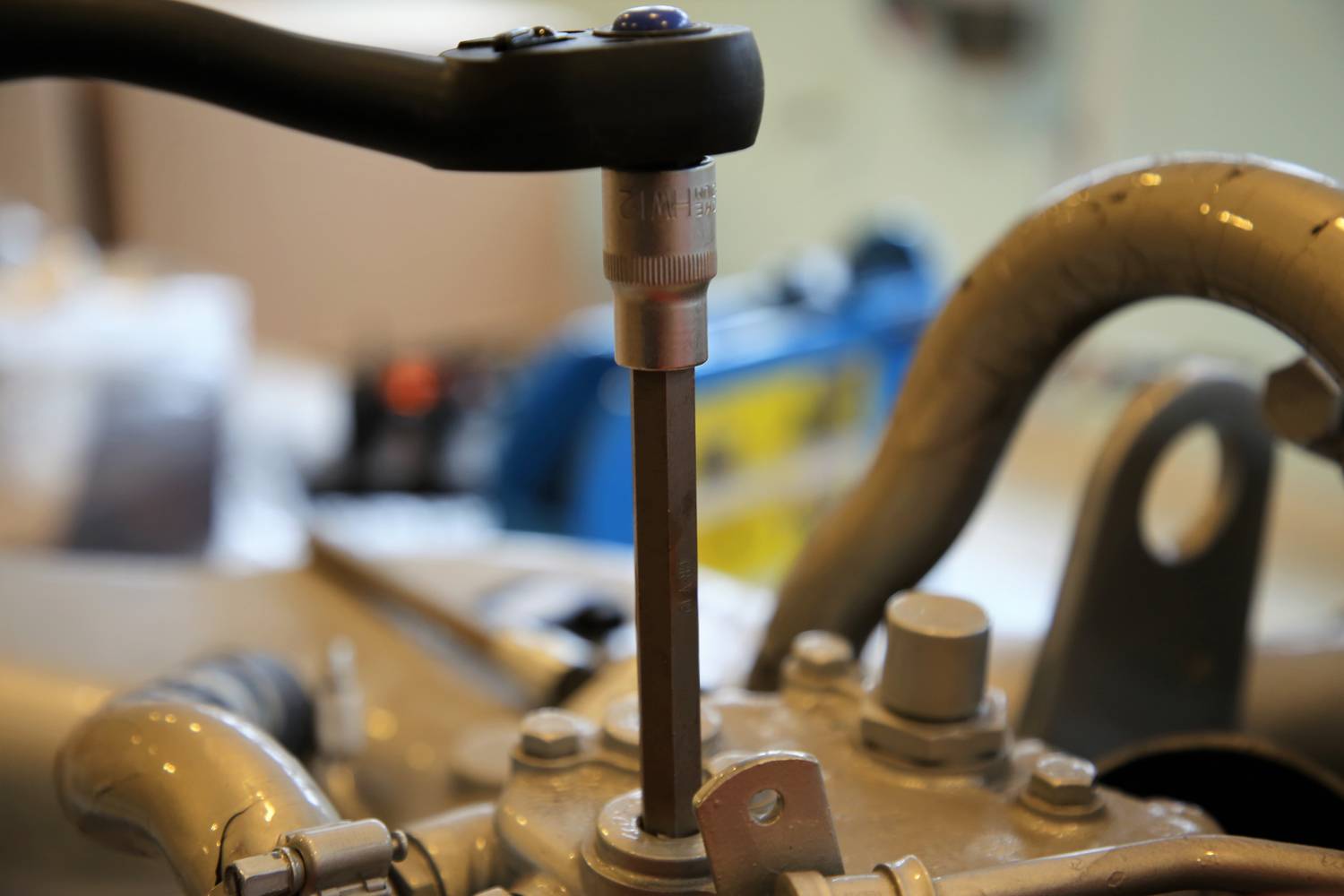 Momentový klíč utahuje šroub na strojním dílu. Důraz je kladen na přesnost a mechaniku.
