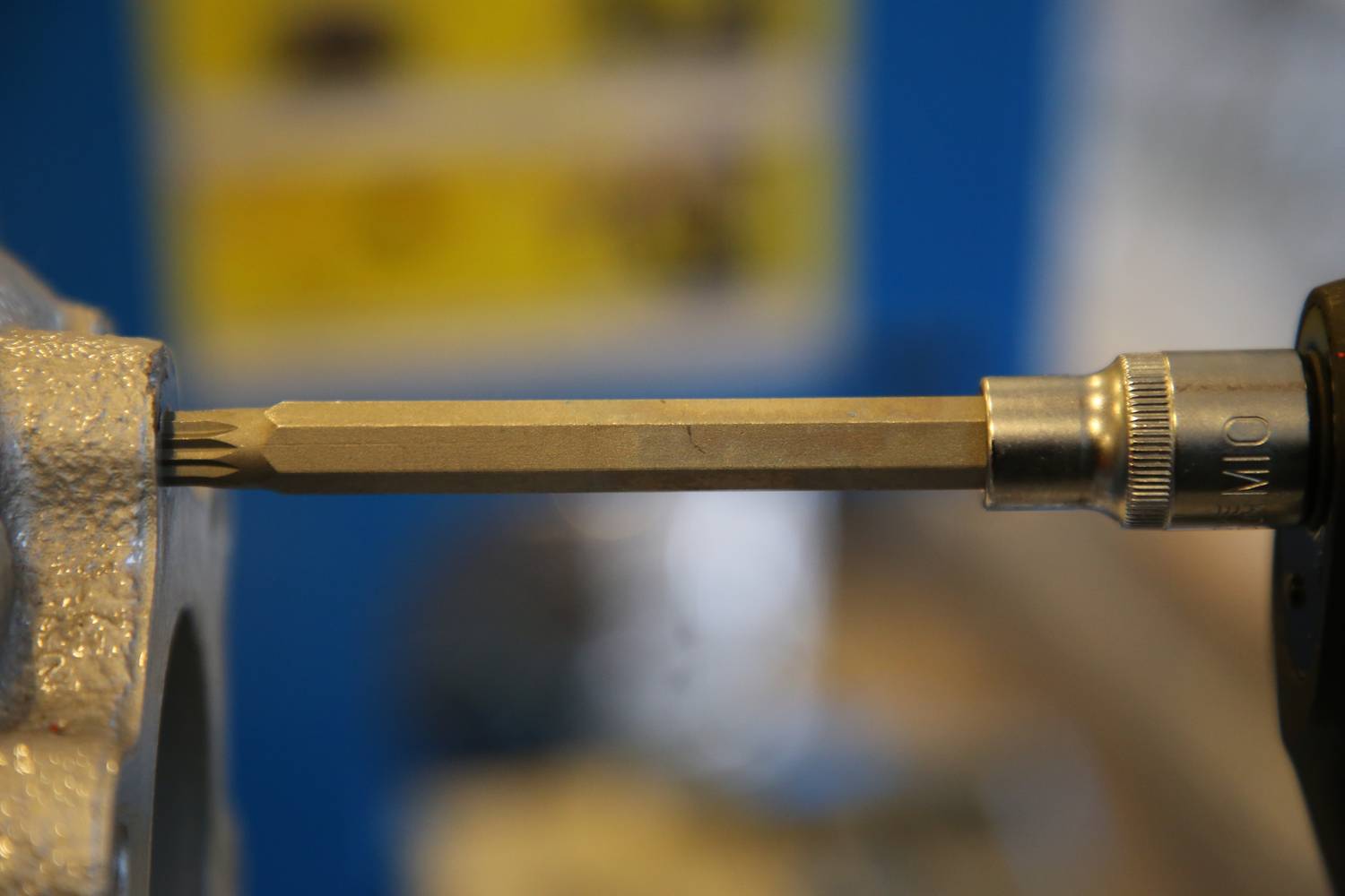 Detailní záběr šroubováku, který zašroubovává šroub do kovové součástky. Zaostřeno na nástroj a šroub, rozmazané pozadí.