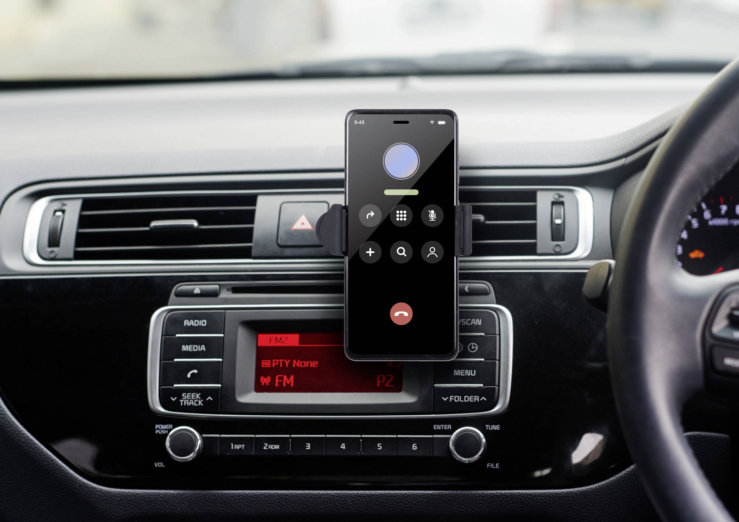 Mobilní telefon je upevněn na palubní desce automobilu a zobrazuje aktivní obrazovku hovoru. Pod ním je autorádio.