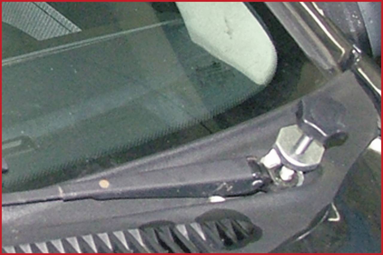 Detailní záběr stěrače na autoskle. Rameno stěrače je připevněno velkým šroubem.