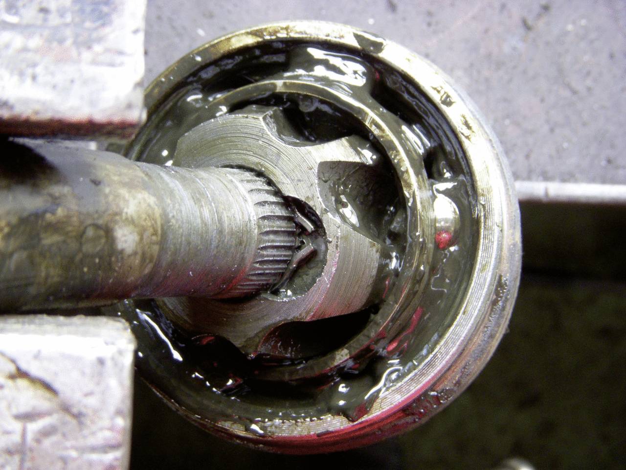 Detailní pohled na kulový kloub, částečně rozložený, s viditelnými ložisky a mazivem, ukazuje mechanické opotřebení a degradaci.
