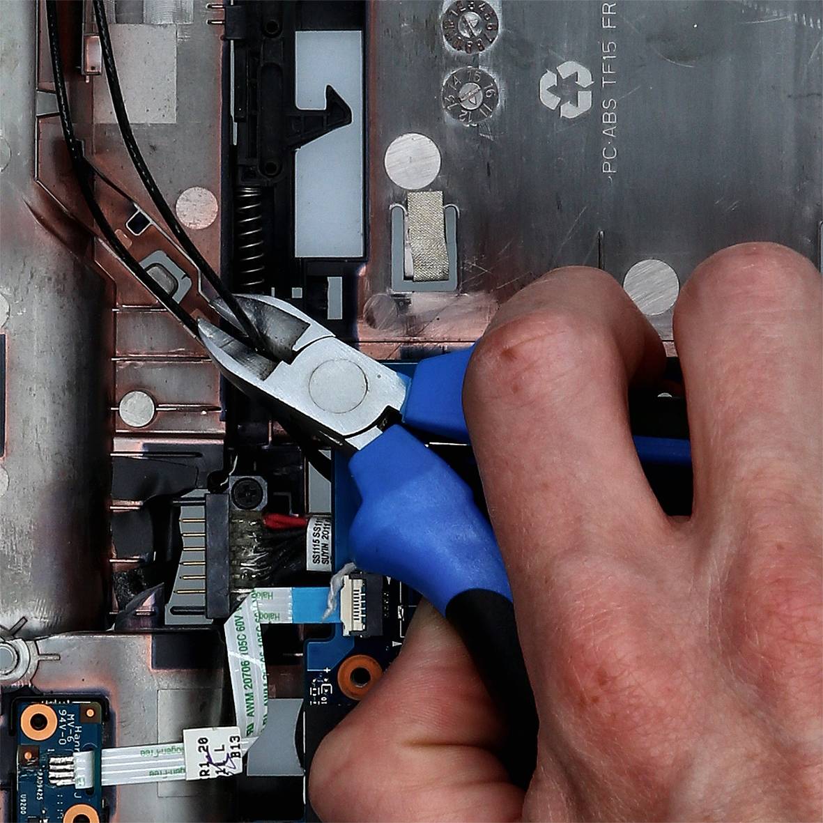 Ruka drží kleště a stříhá kabel uvnitř počítačové skříně. Viditelná základní deska a elektronické komponenty.