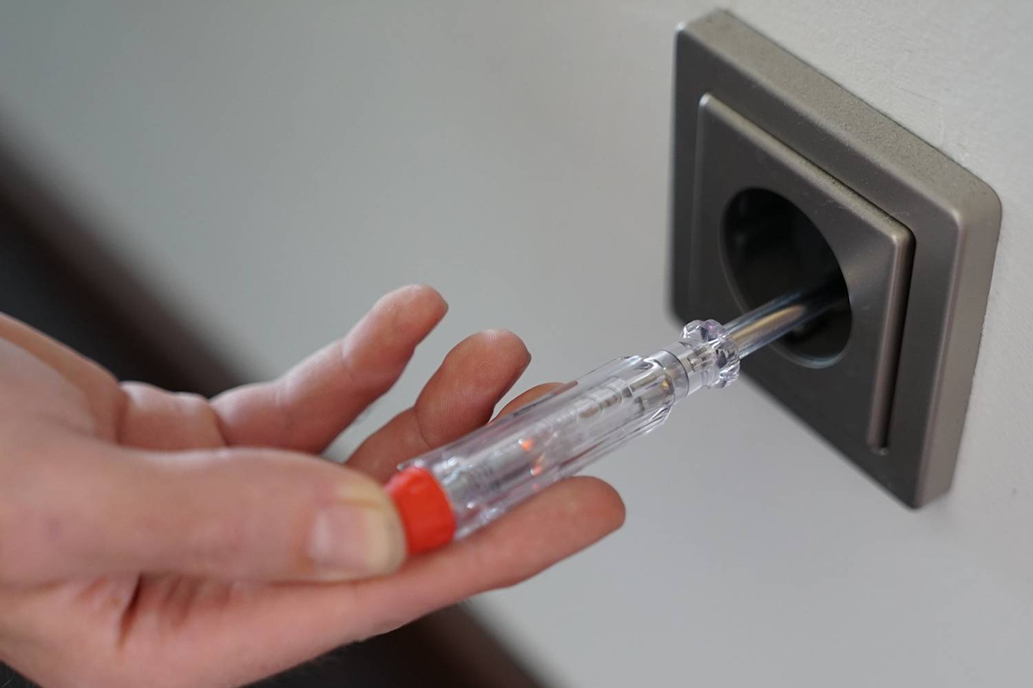 Osoba testuje zásuvku napěťovým testerem, aby zkontrolovala elektrické napětí.