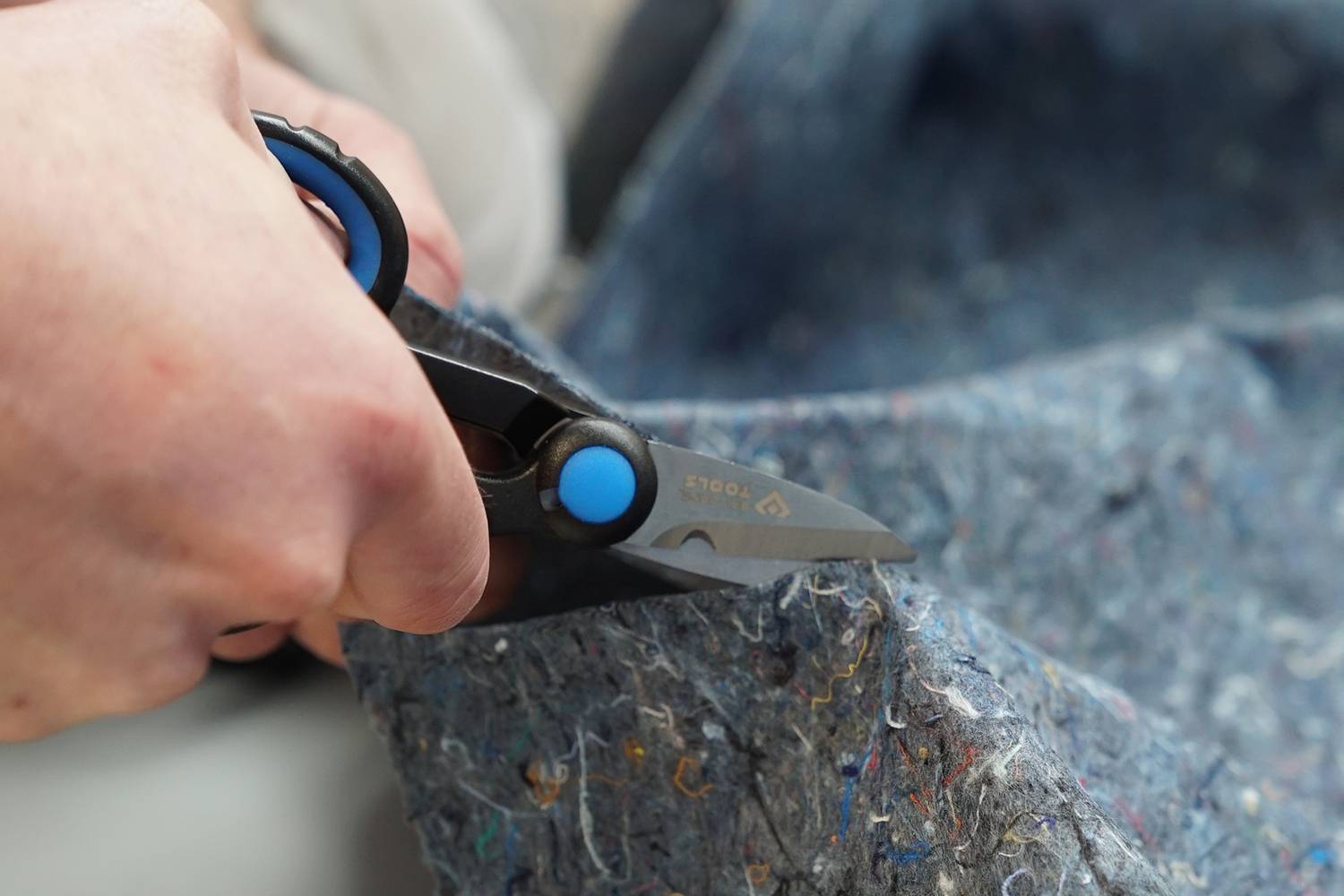 Jedna osoba stříhá tlustý šedý textilní materiál nůžkami.