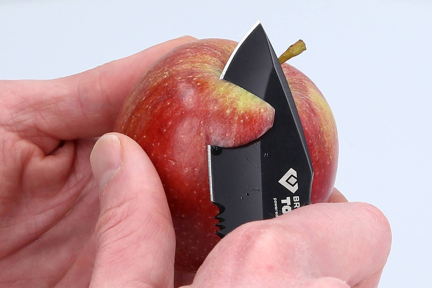 Ruce loupou červené jablko kapesním nožem.