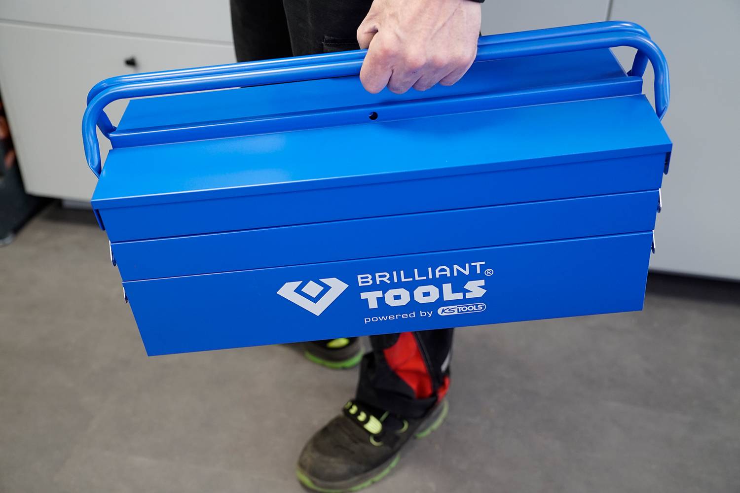 Jedna osoba drží modrý kufřík na nářadí značky 'BRILLIANT TOOLS'.
