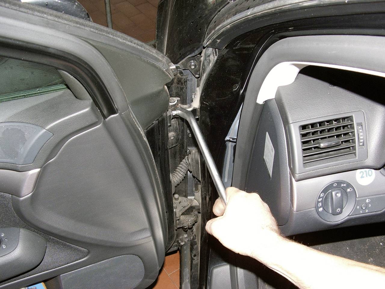 Jedna ruka drží klíč, který je přiložen k místu kloubu na autových dveřích.