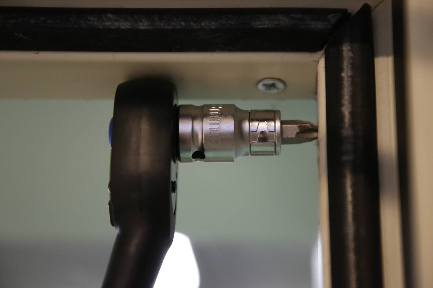 Ráčnový nástroj zatahuje šroub do kovové hrany. Zobrazuje mechanickou práci na konstrukci nebo zařízení.