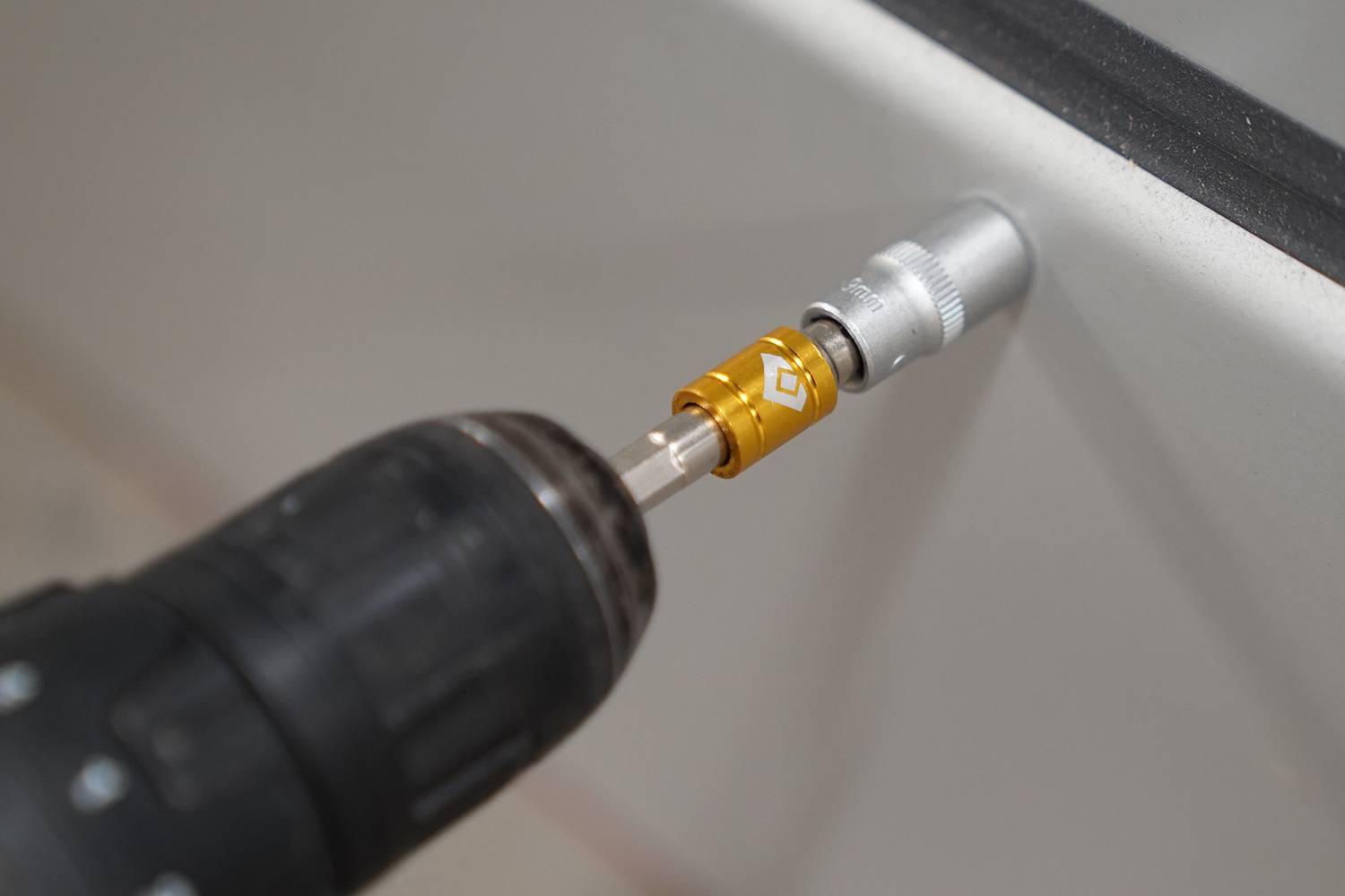 Vrtačka zavádí šroub do bílého povrchu. Hlavice vrtáku je zlatá.