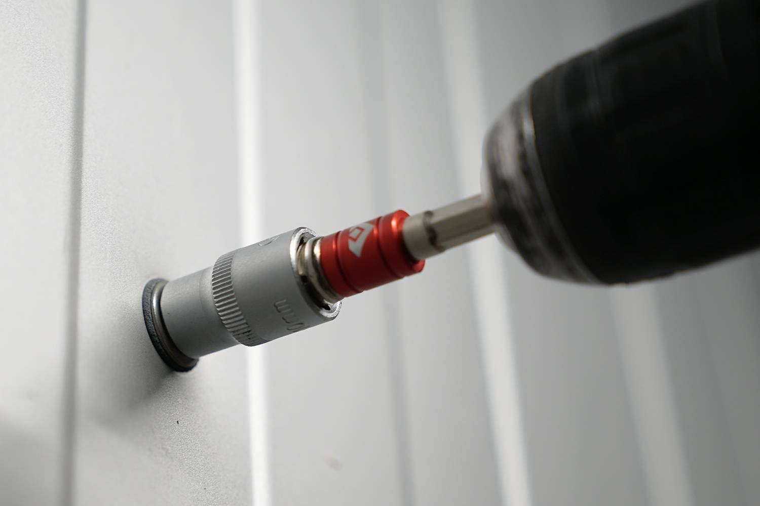 Akumulátorový šroubovák zatahuje šroub do kovové stěny a ukazuje použití elektrického nářadí při stavebních nebo montážních pracích.