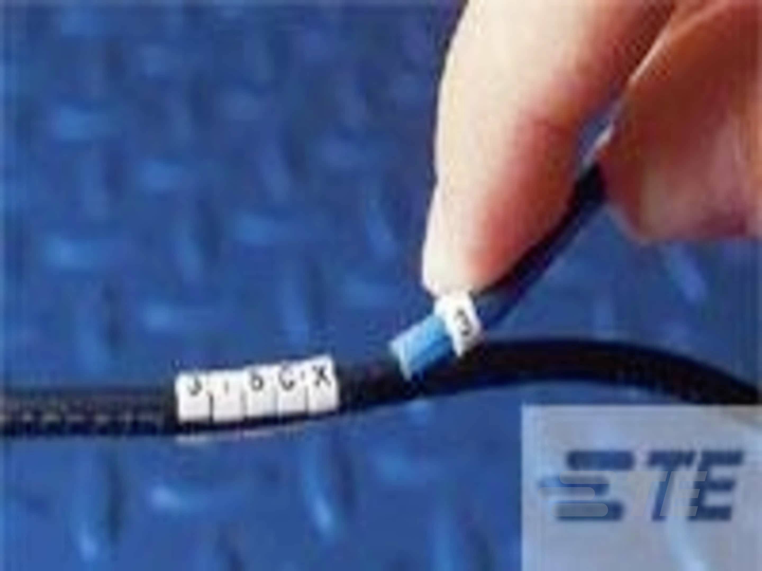 Jedna ruka drží černý kabel, který je opatřen bílými značkami na kabelu a modrým štítkem. V pozadí je viditelné logo.