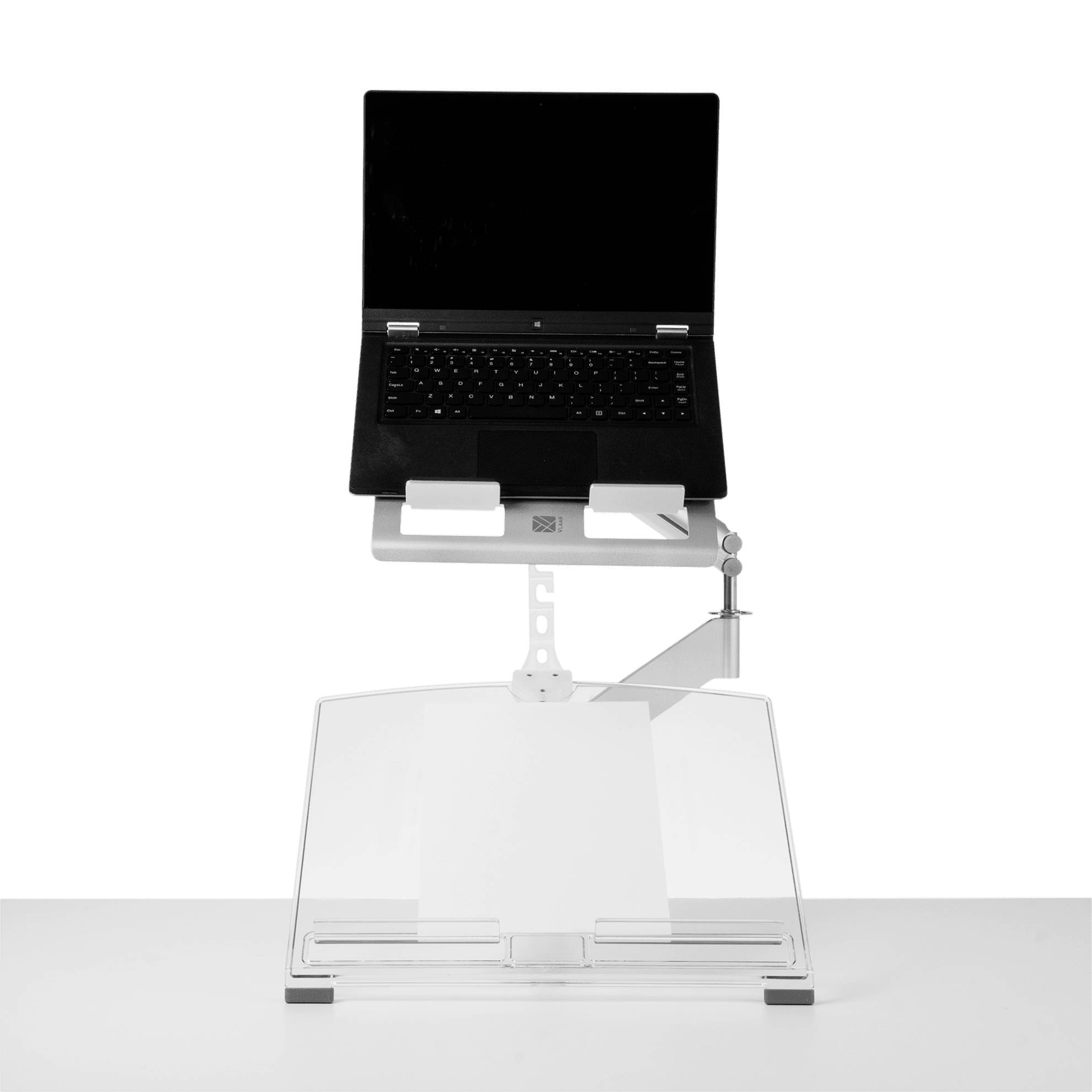 Laptop stojí na výškově nastavitelném stojanu s odkládací plochou pro dokumenty. Ideální pro ergonomickou práci.