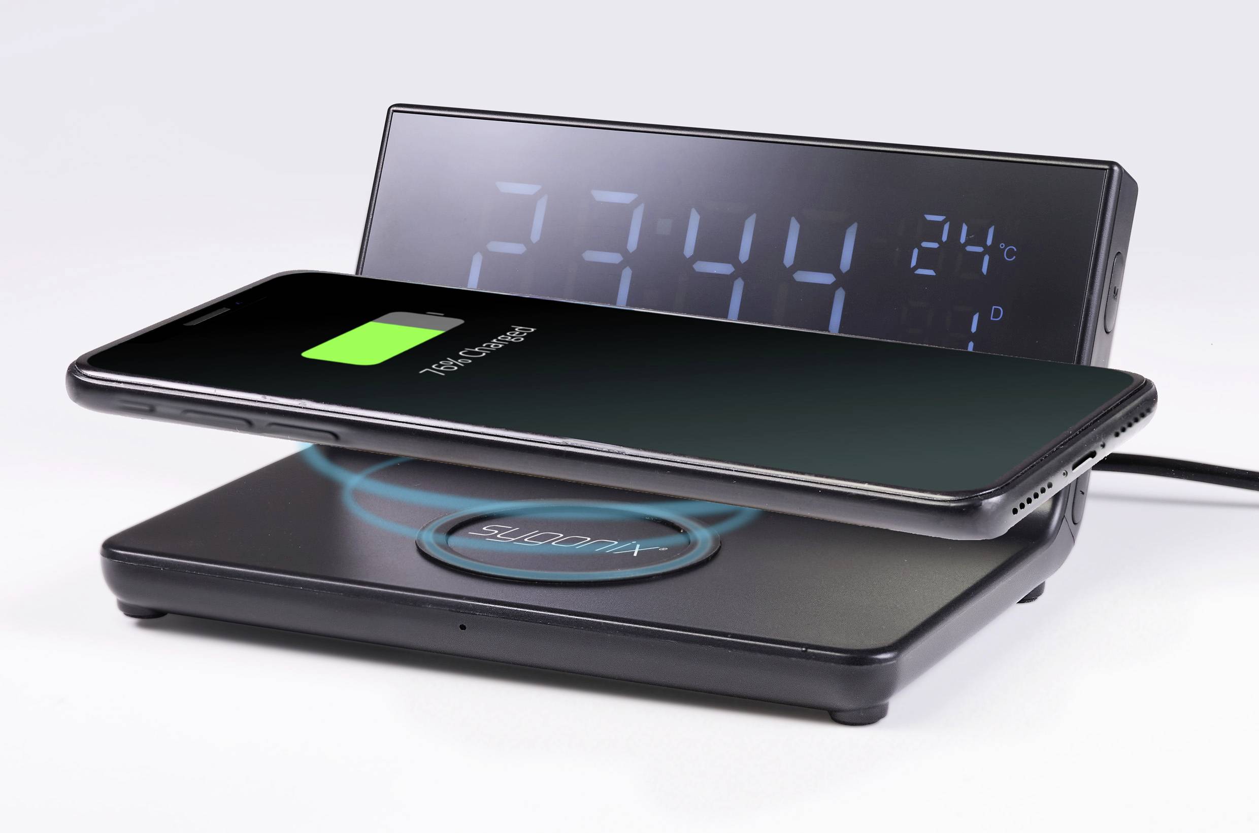 Mobilní telefon se bezdrátově nabíjí na nabíjecí podložce. V pozadí digitální hodiny ukazují čas '23:44' a teplotu '24°C'.
