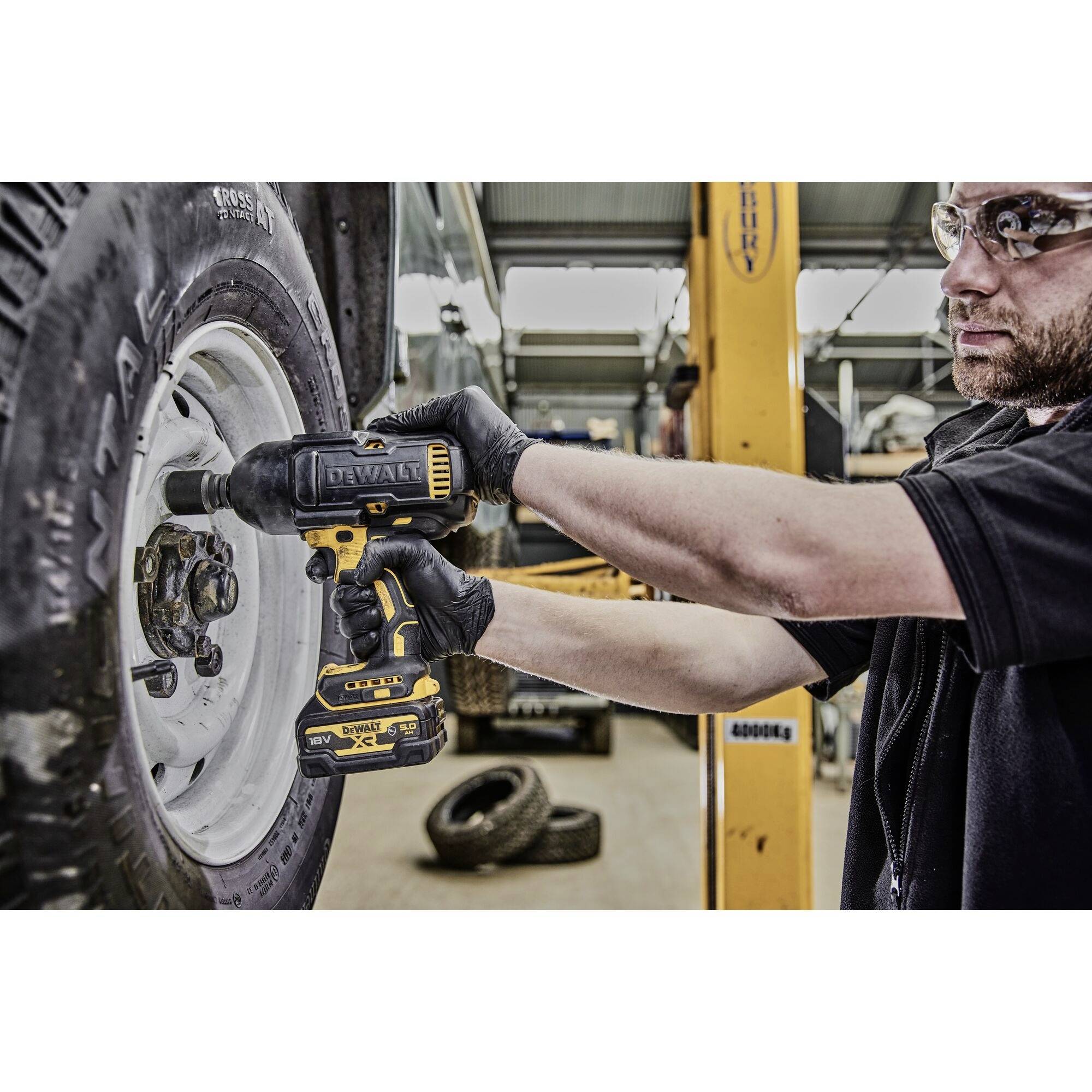 Mechanik používá akumulátorový šroubovák k utažení kol automobilu v autoservisu. Ochranné vybavení je použito.