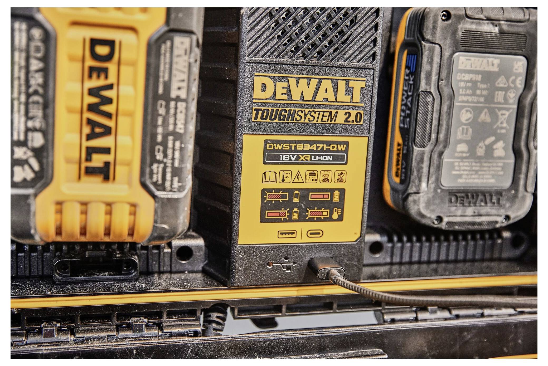 Nabíjecí stanice DeWalt Toughsystem 2.0 s několika pozicemi pro akumulátory, jeden je nabitý, ostatní akumulátory jsou umístěné vedle něj.