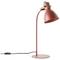 Červená stolní lampa s ohnutým krkem a kulatou základnou; zapnutá a připojená do sítě se spínačem na kabelu.