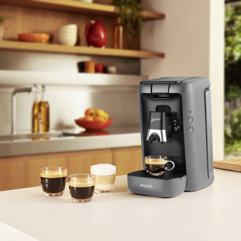 Kávový přístroj na kuchyňské lince připravuje espresso. Vedle něj stojí dvě šálky espresa a jedna šálka mléčné pěny.