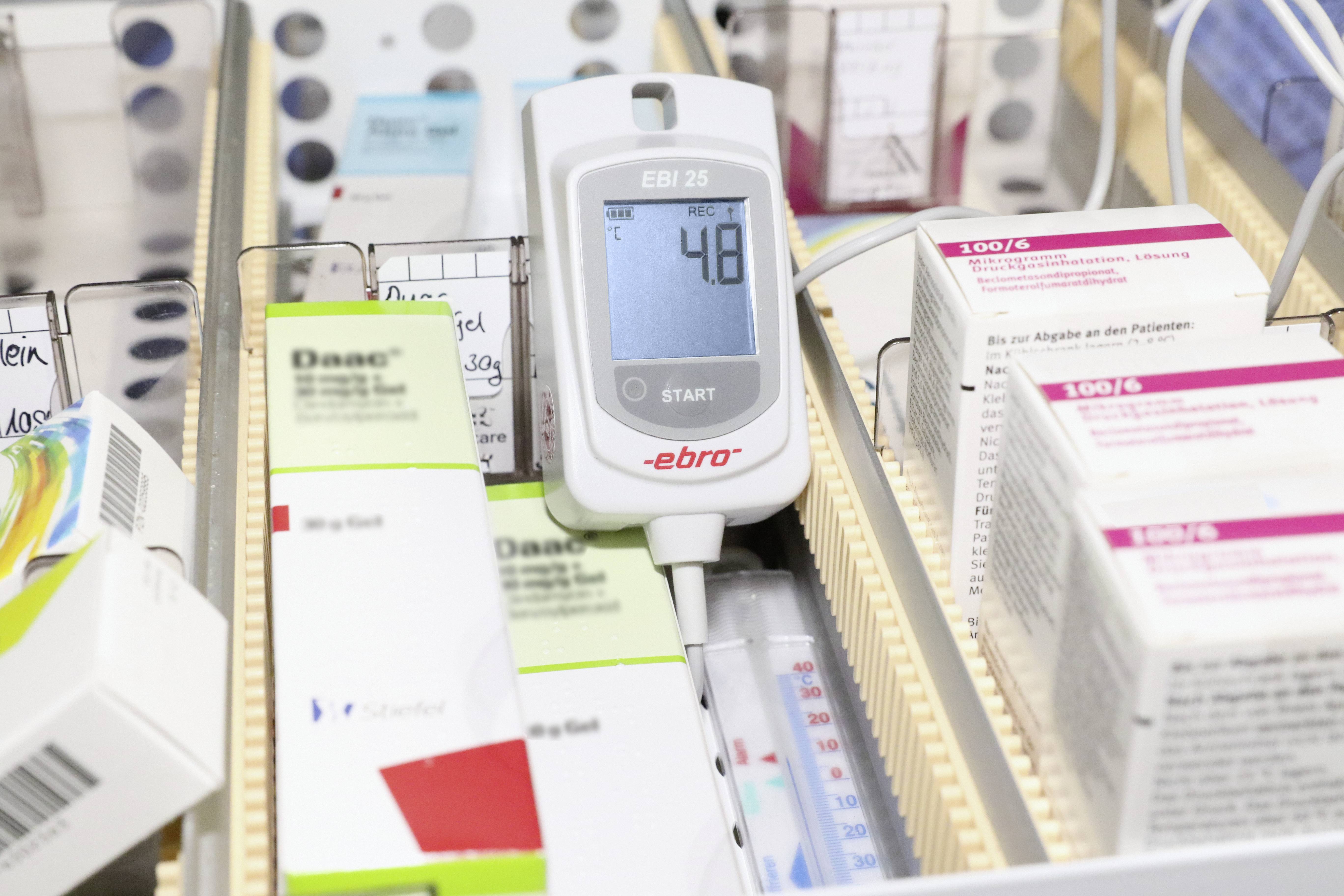 Elektronické měřicí zařízení ukazuje hodnotu '48'. Je obklopeno balením léků a lékařskými záznamy.