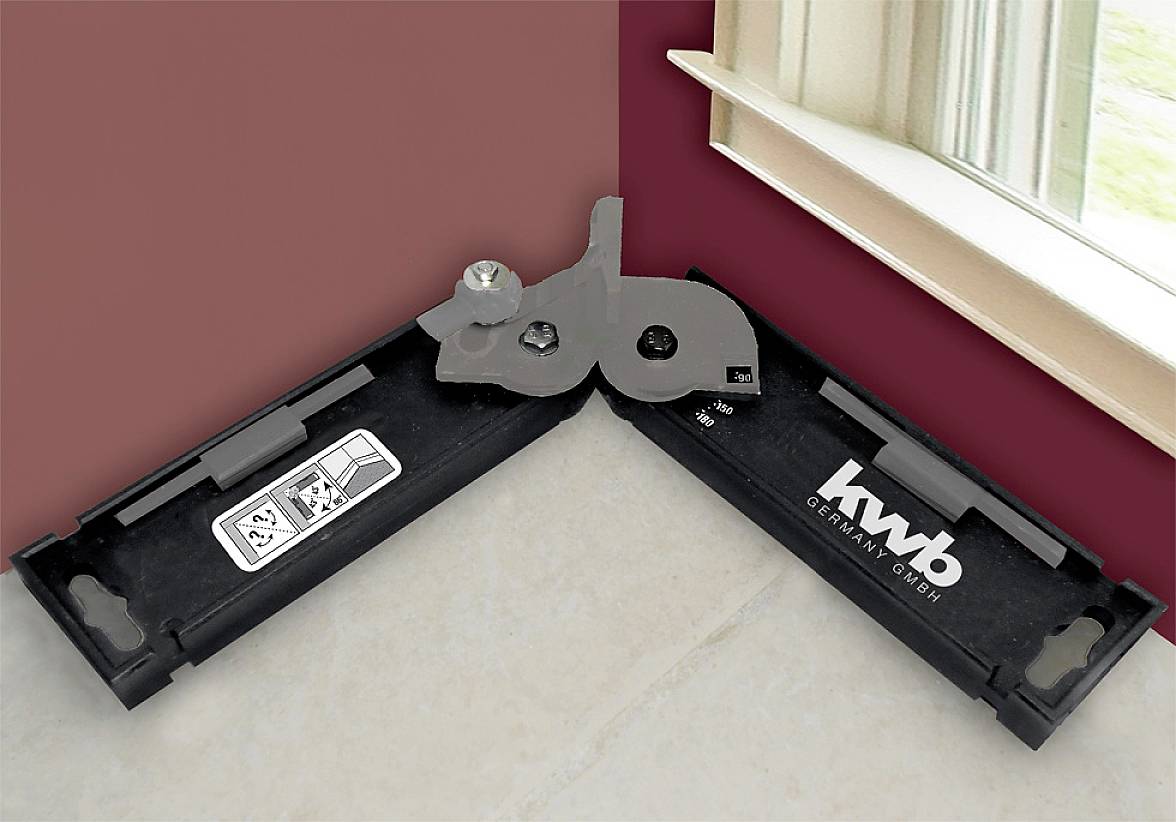 Černé úhlové měřicí pravítko leží v rohu mezi stěnou a podlahou, poblíž okna.