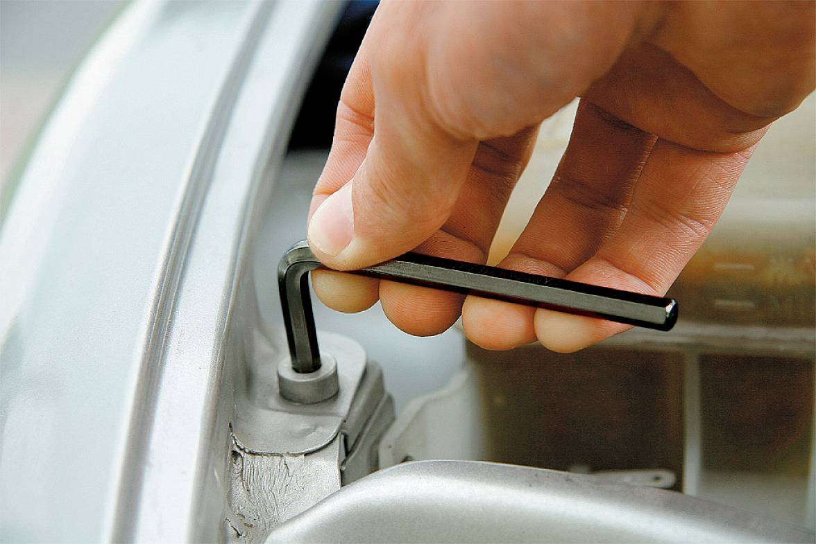 Jedna ruka otáčí šestihranným klíčem šroub na stříbrné součásti automobilu.