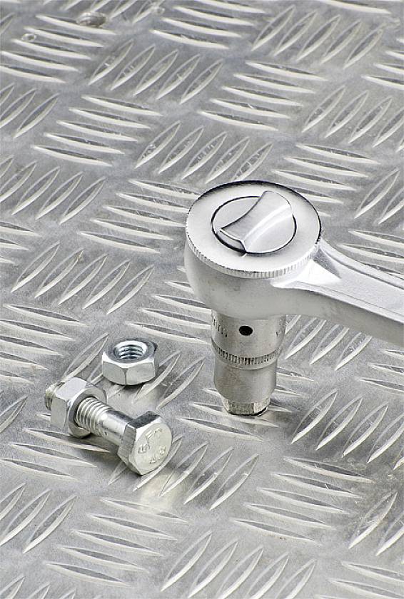 Na kovovém rýhovaném plechu leží ráčna vedle volně položeného šroubu a matice.