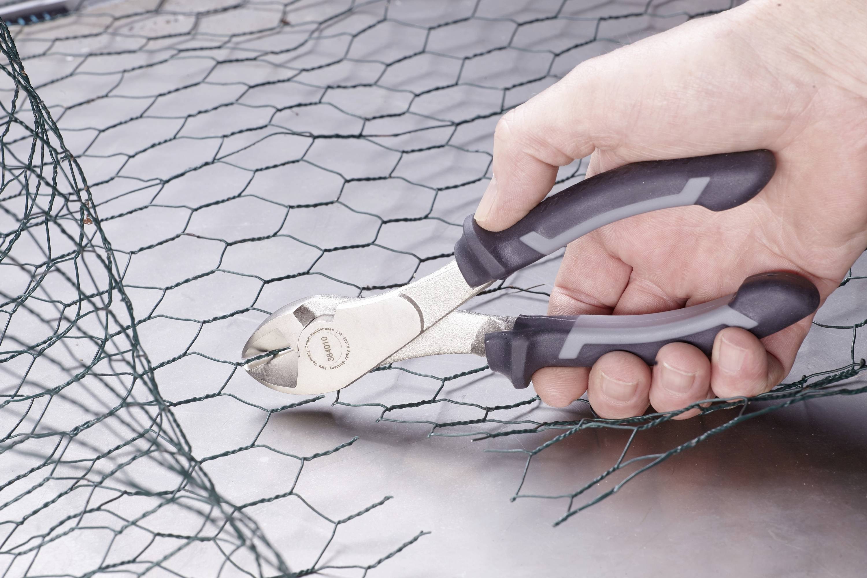 Jedna ruka drží štípací kleště, které řezají pletivo na kovovém povrchu.