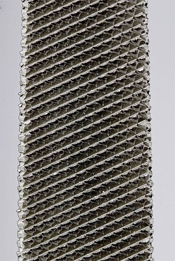 Detailní záběr obdélníkové kovové mřížky s diagonálními drážkami.