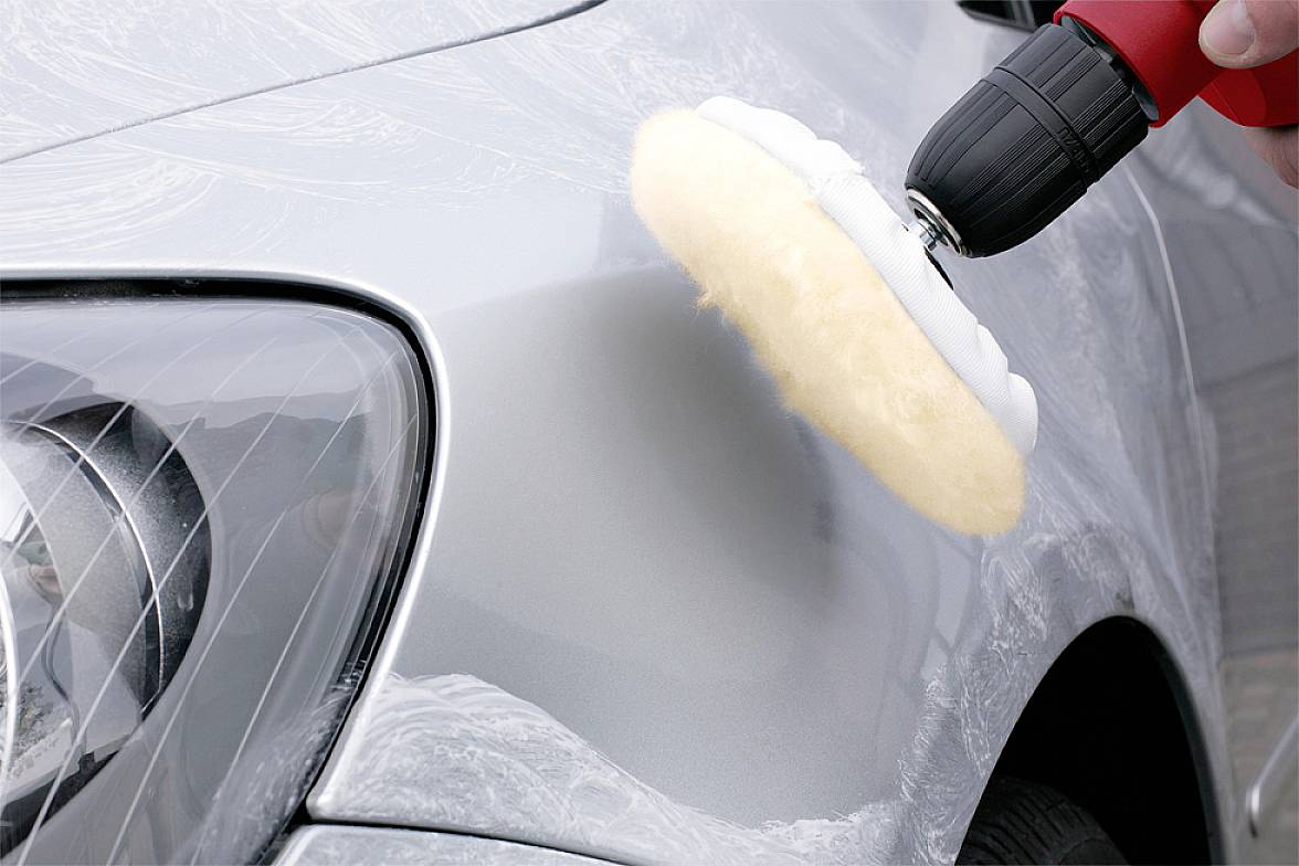 Osoba leští lesklý stříbrný povrch automobilu pomocí rotační leštičky a měkkého lešticího kotouče.