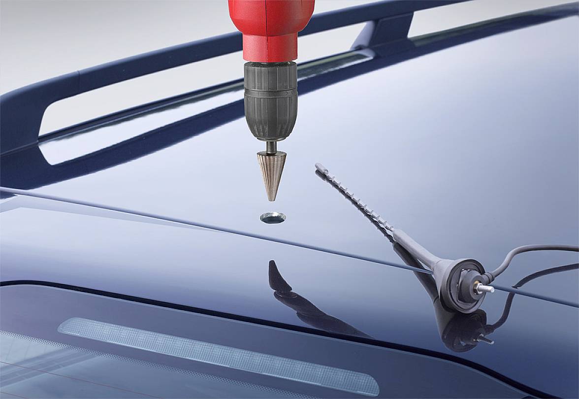 Červená vrtačka vrtá díru do střechy automobilu. Vedle leží šedý šroubovák.