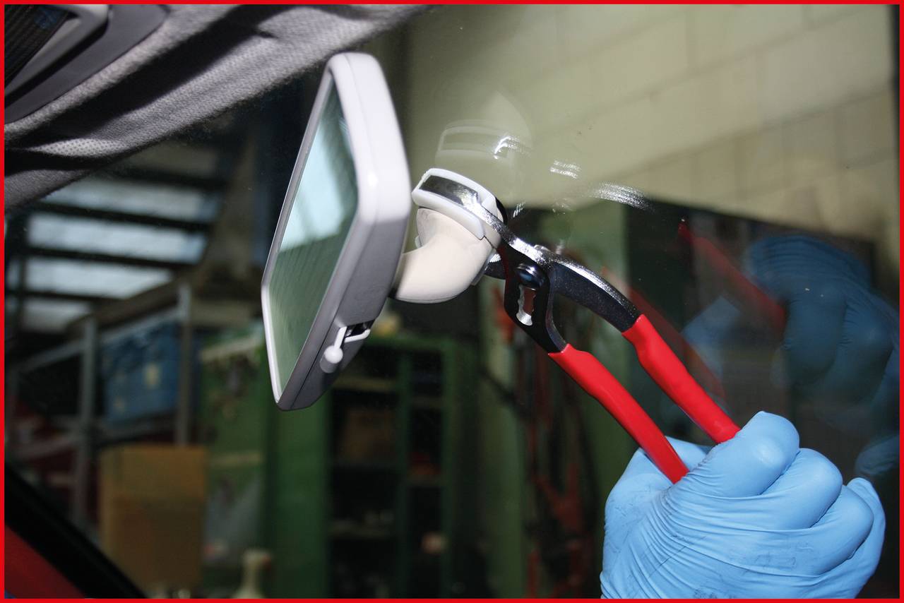 Osoba v modrých rukavicích opravuje zpětné zrcátko automobilem pomocí kleští uvnitř vozu.