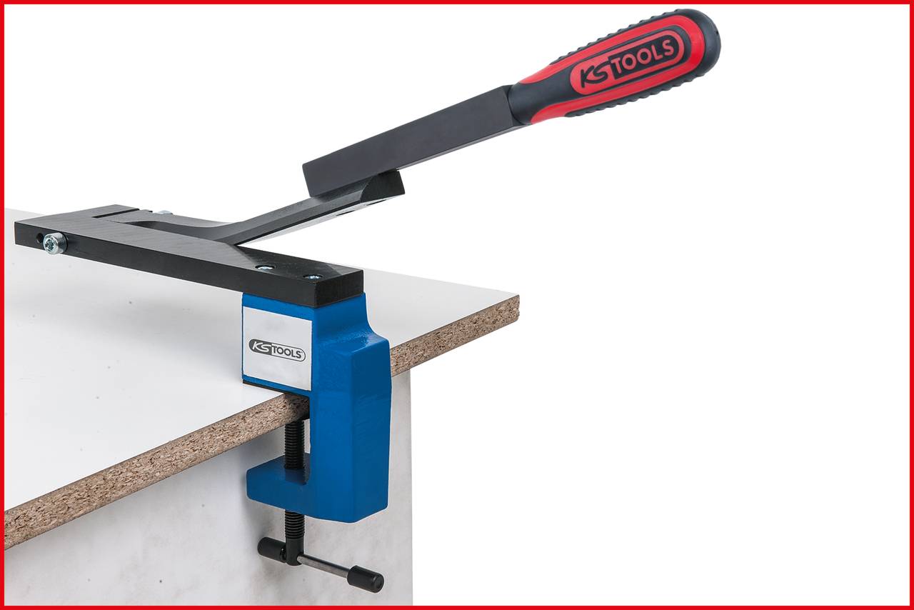 Svěrka na pracovní stůl od KS Tools upevňuje dřevěnou desku na okraji stolu. Červené a černé rukojeti, modrá svorka.
