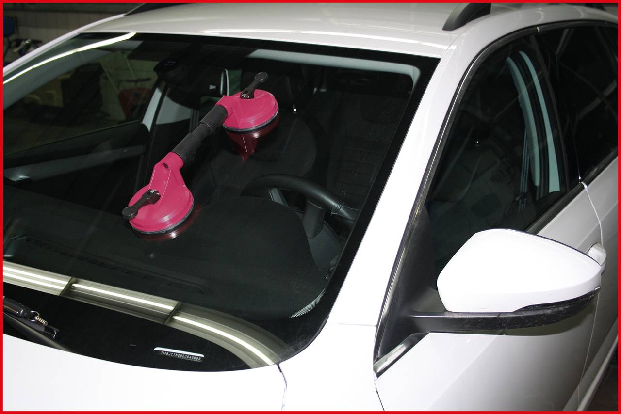 Detailní záběr bílého automobilu se dvěma růžovými přísavkami na čelním skle, které naznačují výměnu nebo opravu.