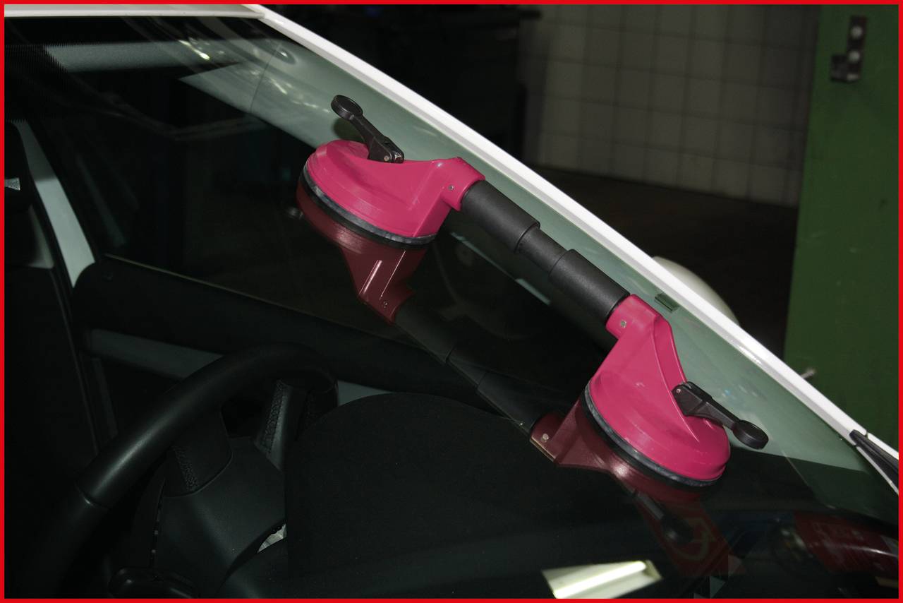Na vnější straně autoskla jsou připevněny dva červené přísavky, pravděpodobně určené pro opravu nebo výměnu skla.